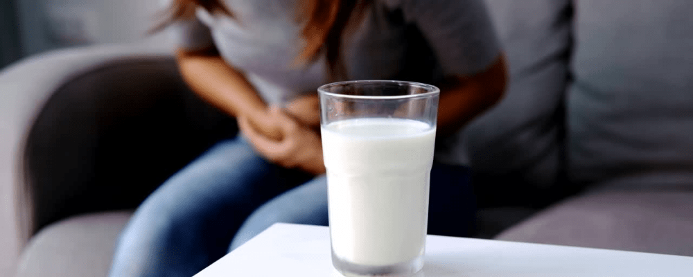 Milch auf dem Tisch und Frau im Hintergrund mit Bauchschmerzen